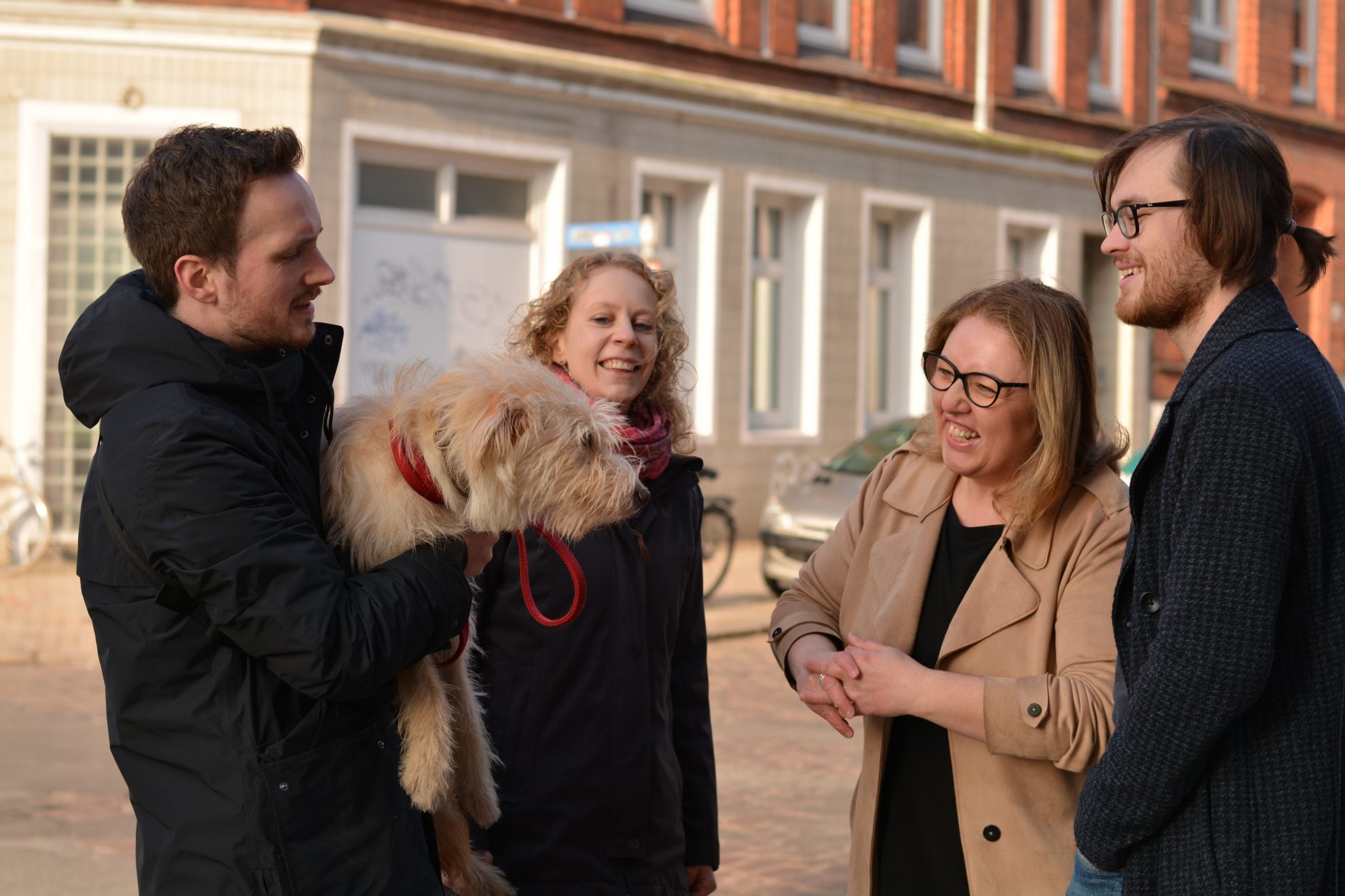 Özlem Ünsal im Gespräch mit drei Personen, von denen eine einen Hund auf dem Arm hat,. Alle sind fröhlich.